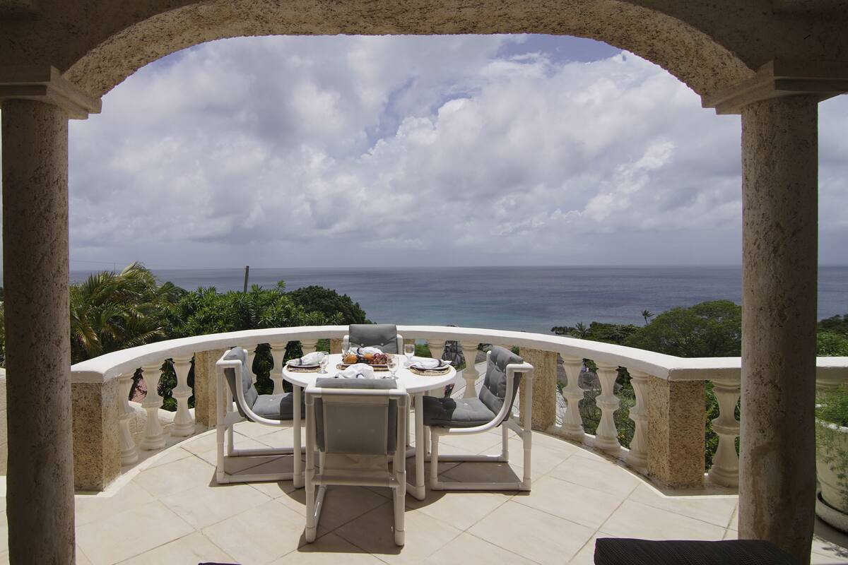 Un balcón con una mesa lista para comer, con vistas a un paisaje marino.