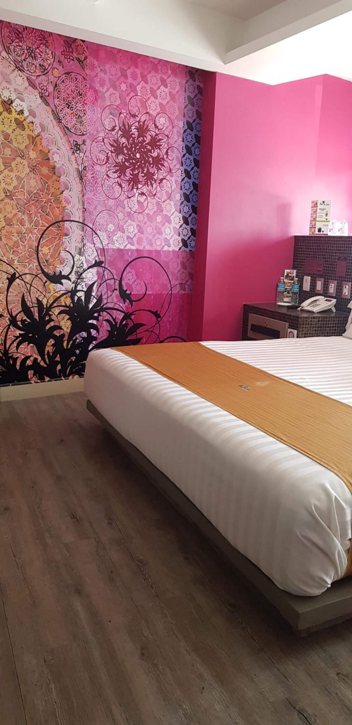 Una habitación de hotel con una cama grande, piso de madera y pared con un llamativo estampado rosa y morado.