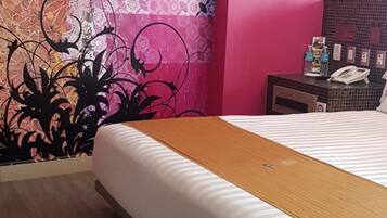 Una habitación de hotel con una cama grande, piso de madera y pared con un llamativo estampado rosa y morado.