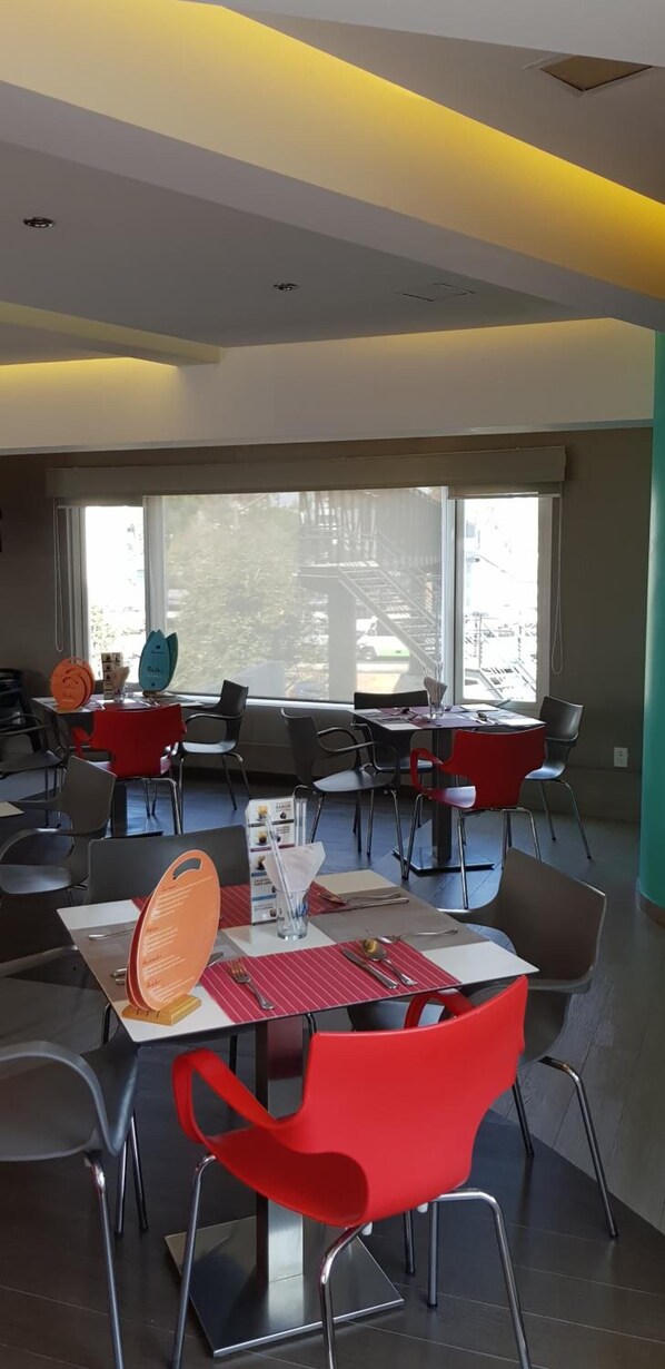 Un comedor moderno con mesas y sillas, ventanas amplias y vistas al exterior.