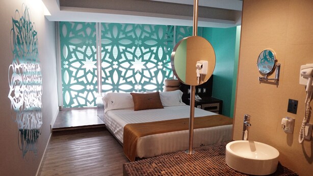 A hotel room with a bed, a large mirror, a sink, and a decorative wall. - Hotel Amala (Mexico City)