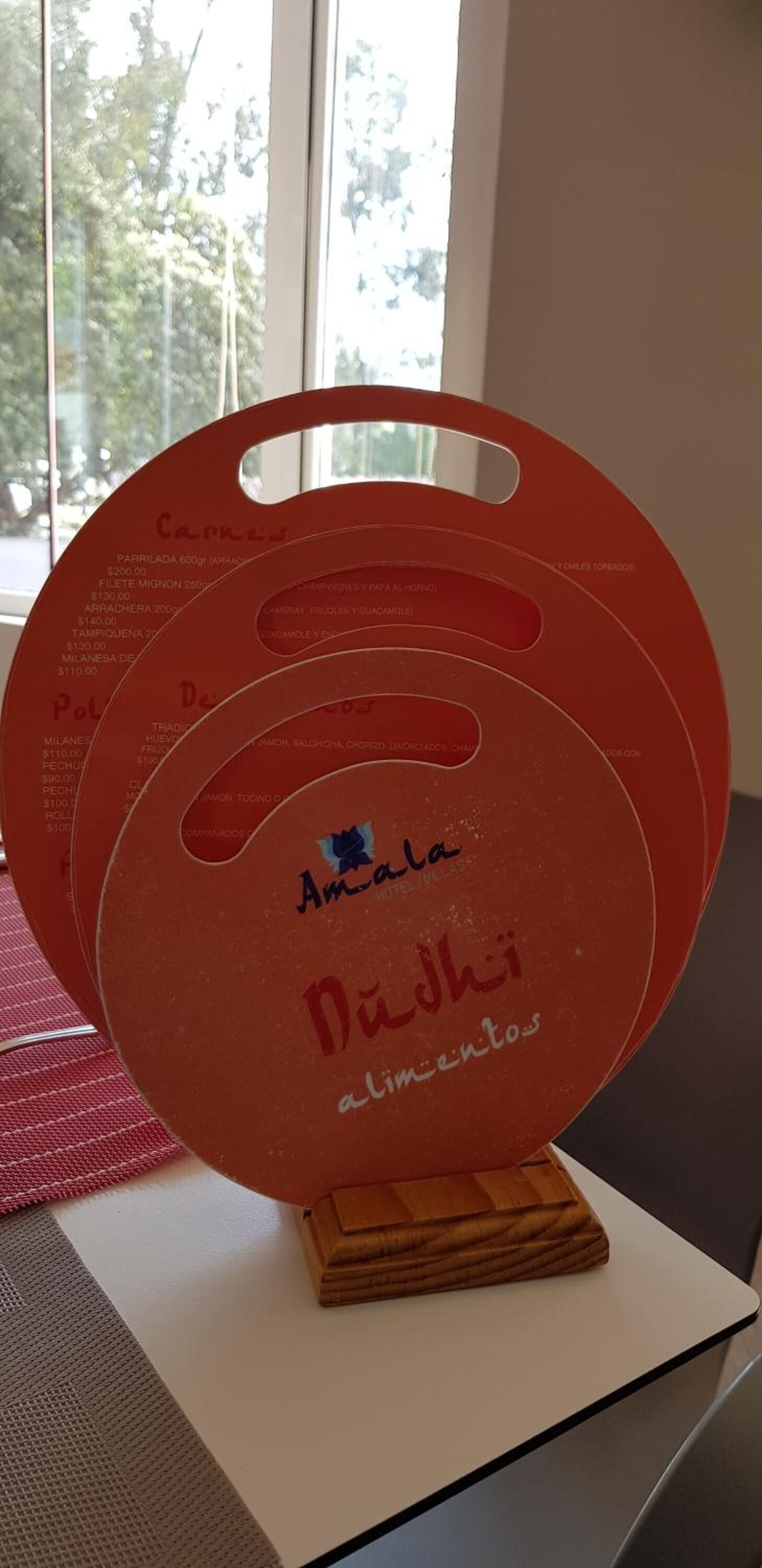 Un menú circular rojo con texto y precios, sobre un soporte de madera.