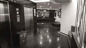 A modern elevator with a control panel, a polished floor, and a reception area with a counter and decorative wall art. - Hotel Amala (Mexico City)