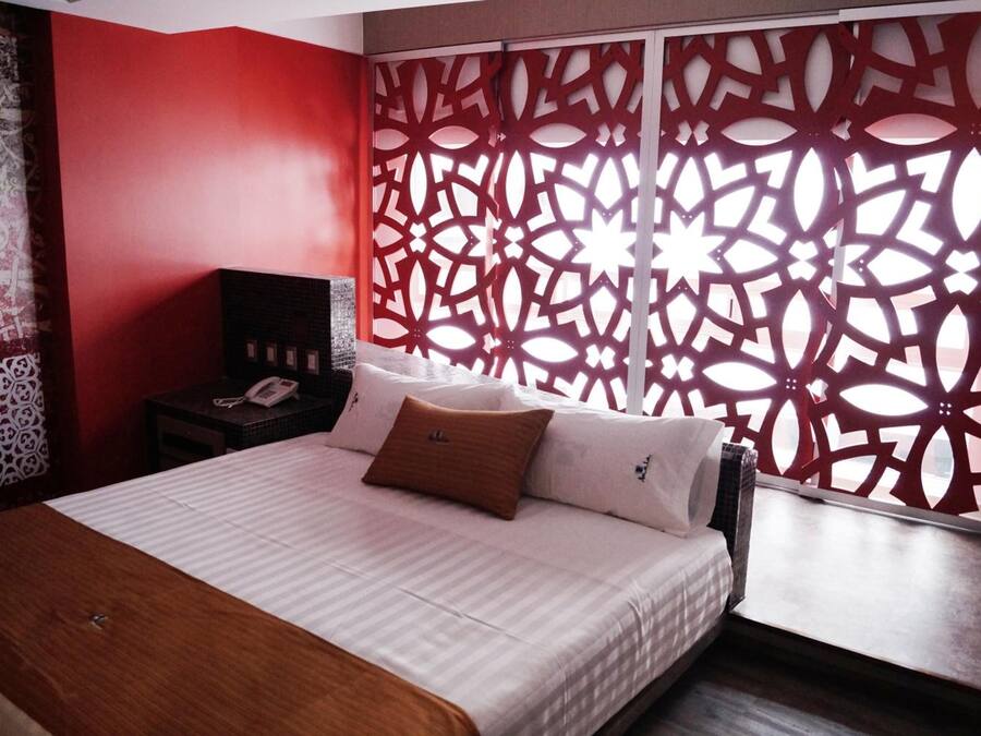 Ein Hotelzimmer mit einem Bett, einem Nachttisch mit Telefon und einem roten dekorativen Raumteiler.