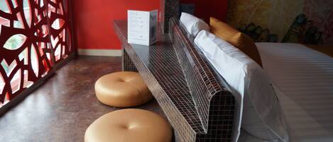 A hotel room with a bed, two round ottomans, a decorative wall, and a red partition.