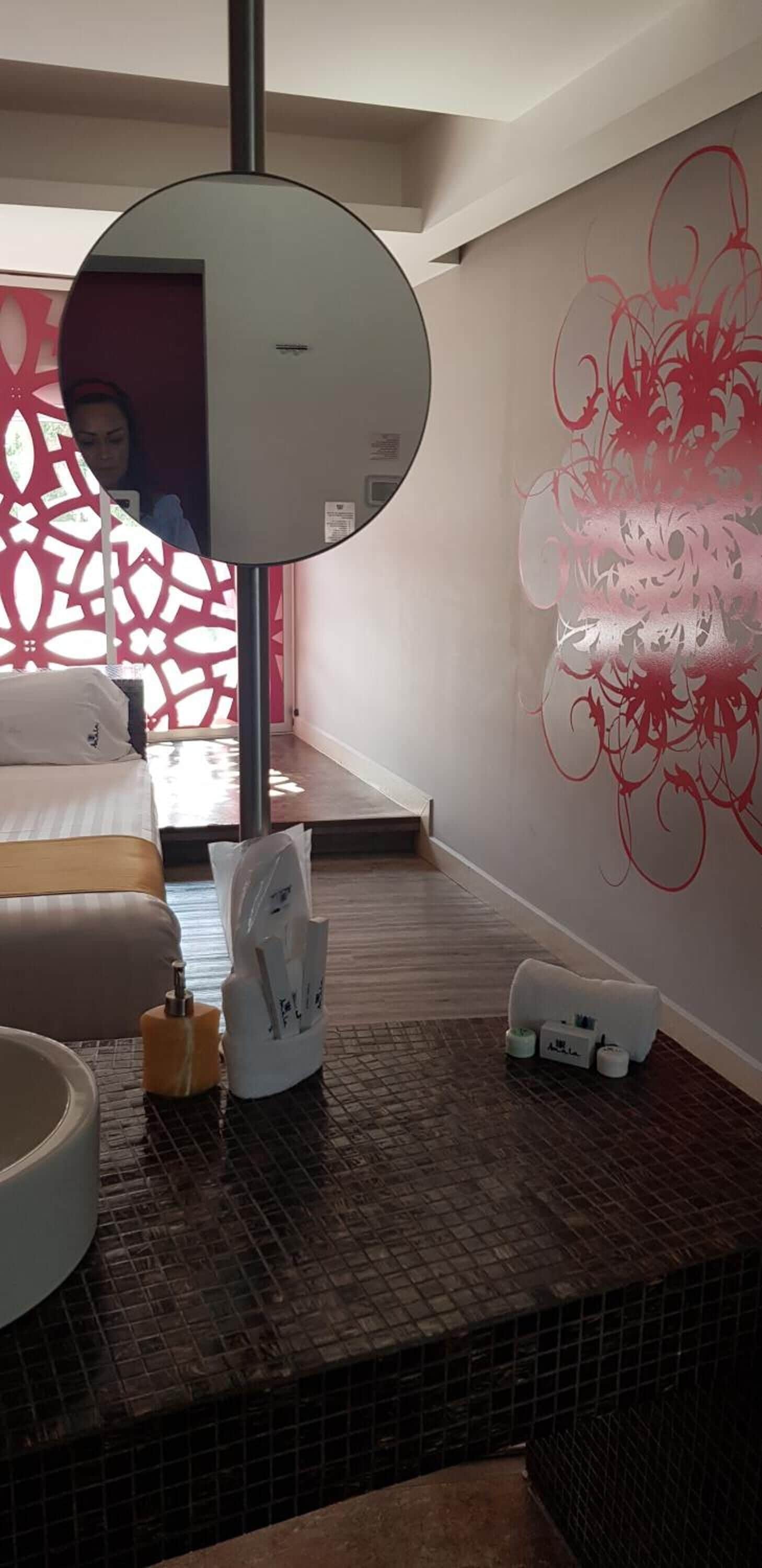 Una habitación de hotel con un espejo grande, una cama, un baño con lavamanos y un adornado en la pared.