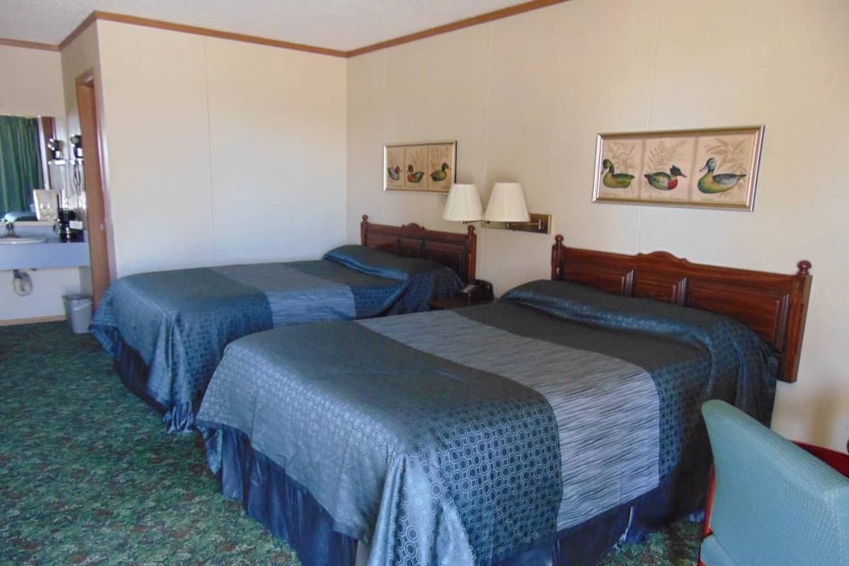 A hotel room with two beds, a desk with a chair, a mirror, and two wall-mounted lamps.