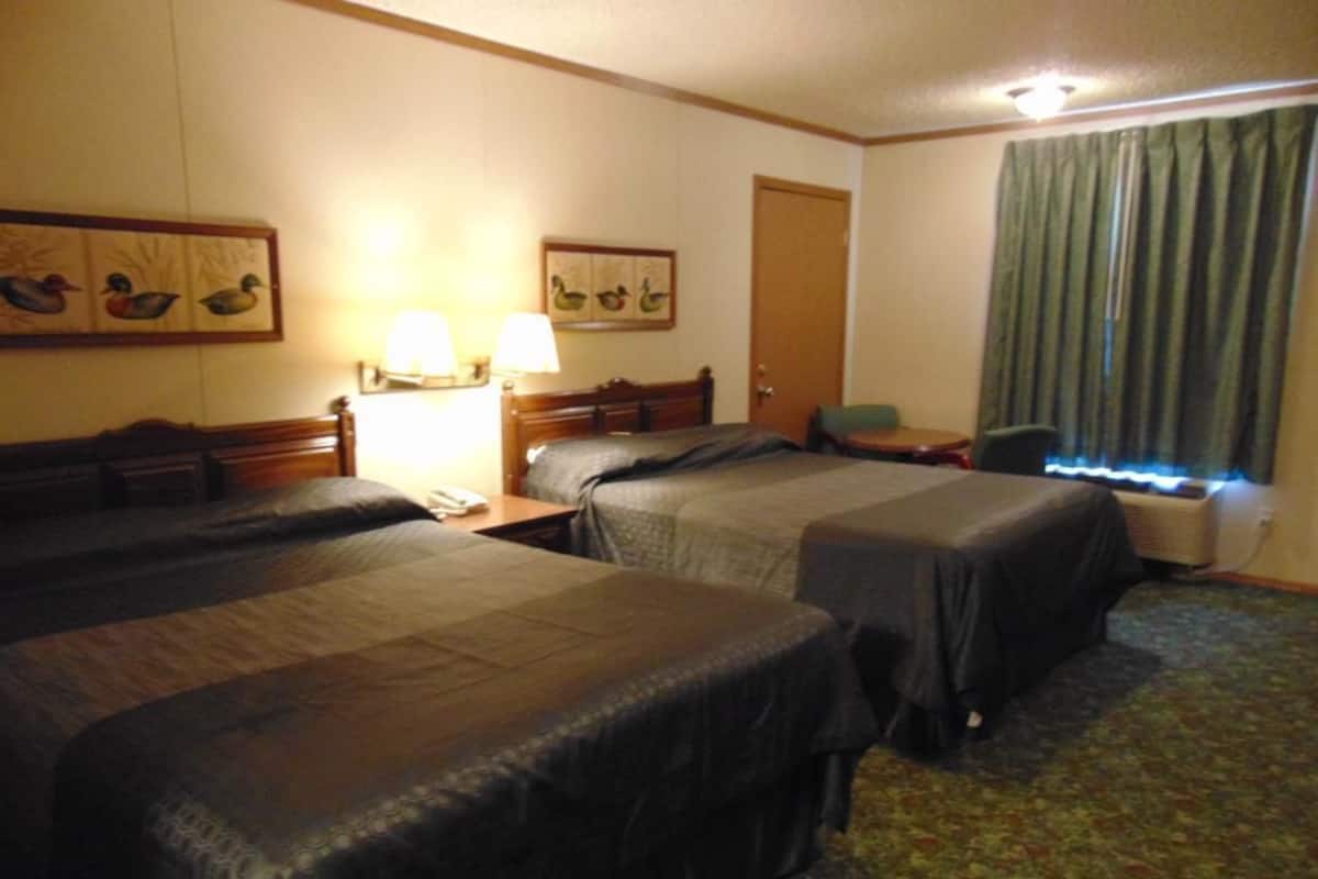 A hotel room with two beds, a desk, a chair, a lamp, and a window with curtains.