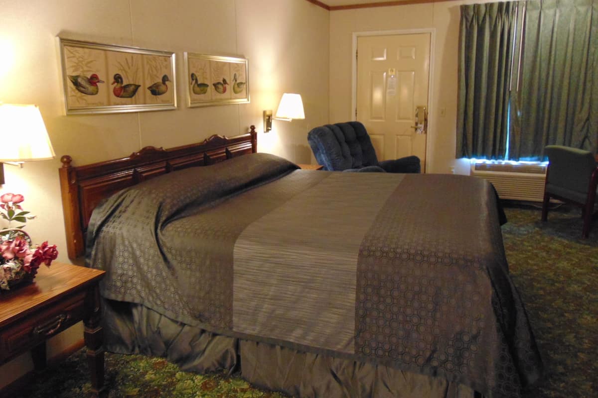 A hotel room with a large bed, a chair, a desk with a lamp, and wall art.