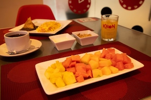 A dining table with a plate of cubed fruit, a cup of coffee, and a glass of orange juice. - Love Hotel Kron (Mexico City)
