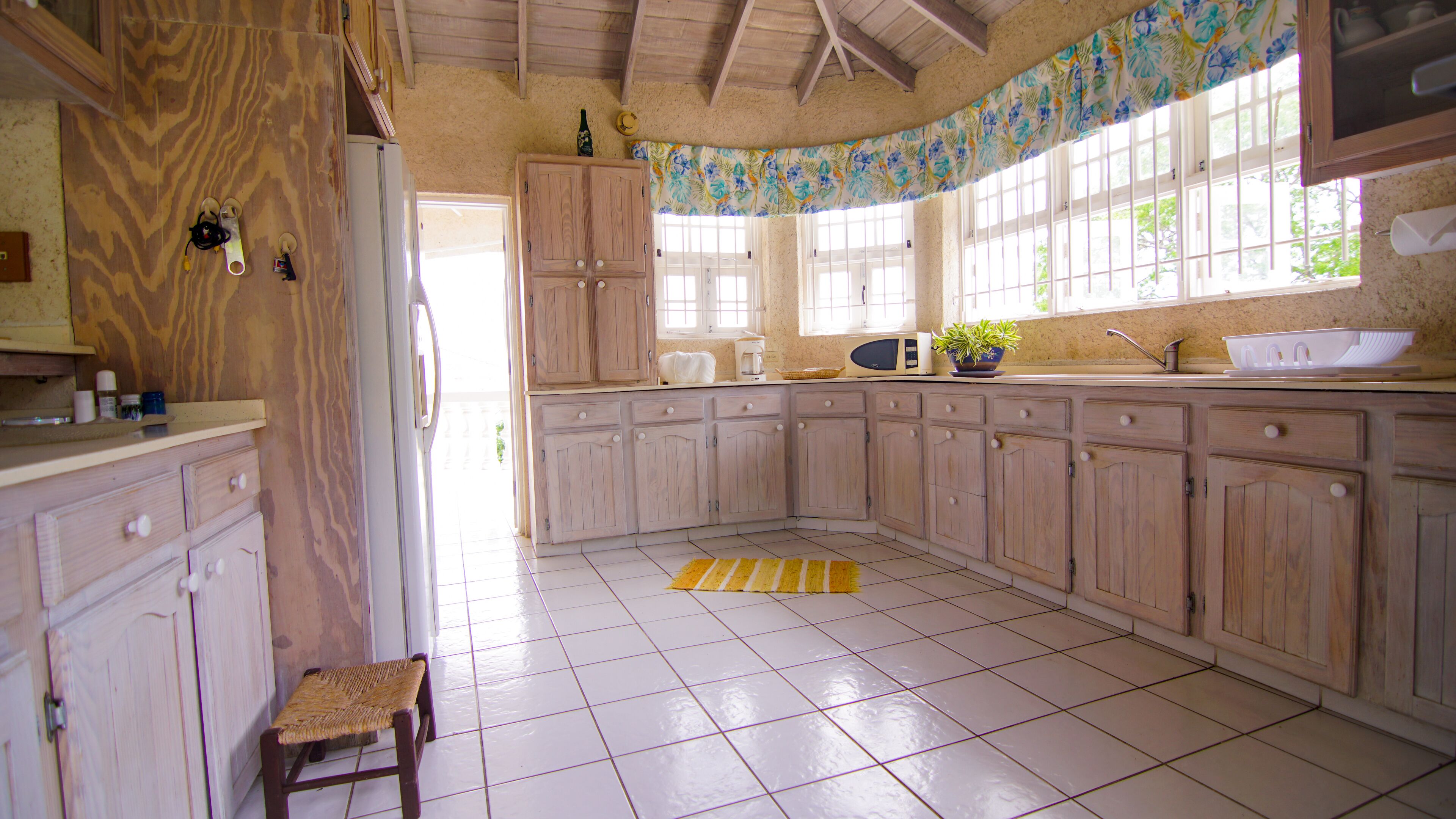 A kitchen with wooden cabinets, a microwave, a sink, and a window with a floral curtain.
