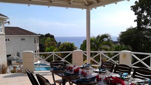 An outdoor dining area with a view of the sea, white railing, and a pool in the background. - Sea Symphony Villa (Fryers Well)