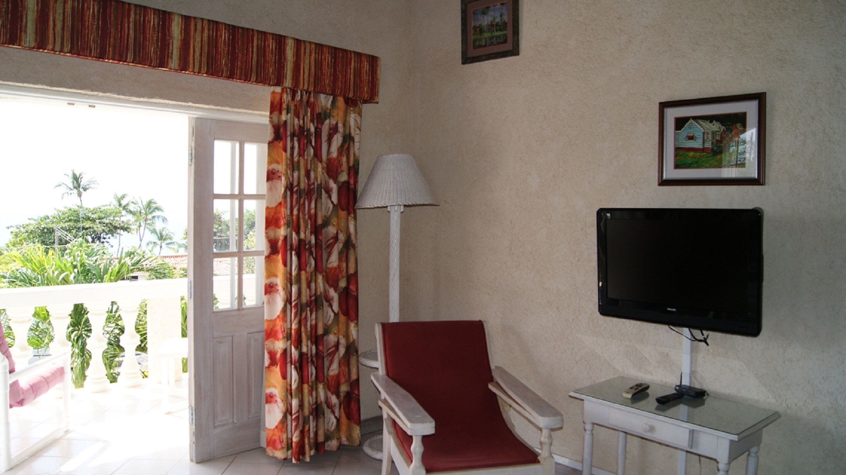 Een kamer met een televisie, een stoel, een lamp en een deur naar een balkon.