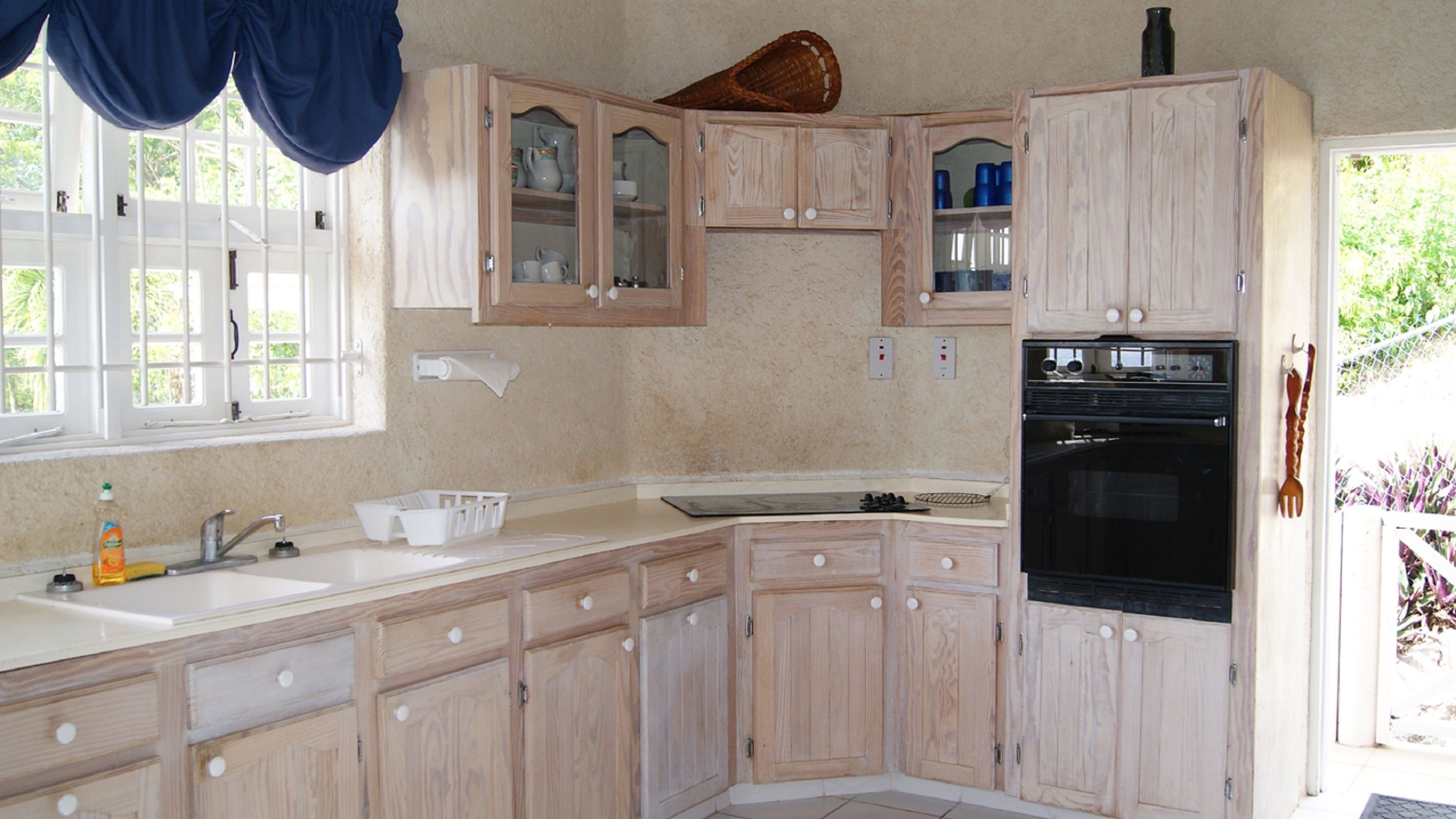 Una cocina con armarios de madera, un lavamanos, una estufa y una ventana con cortinas.