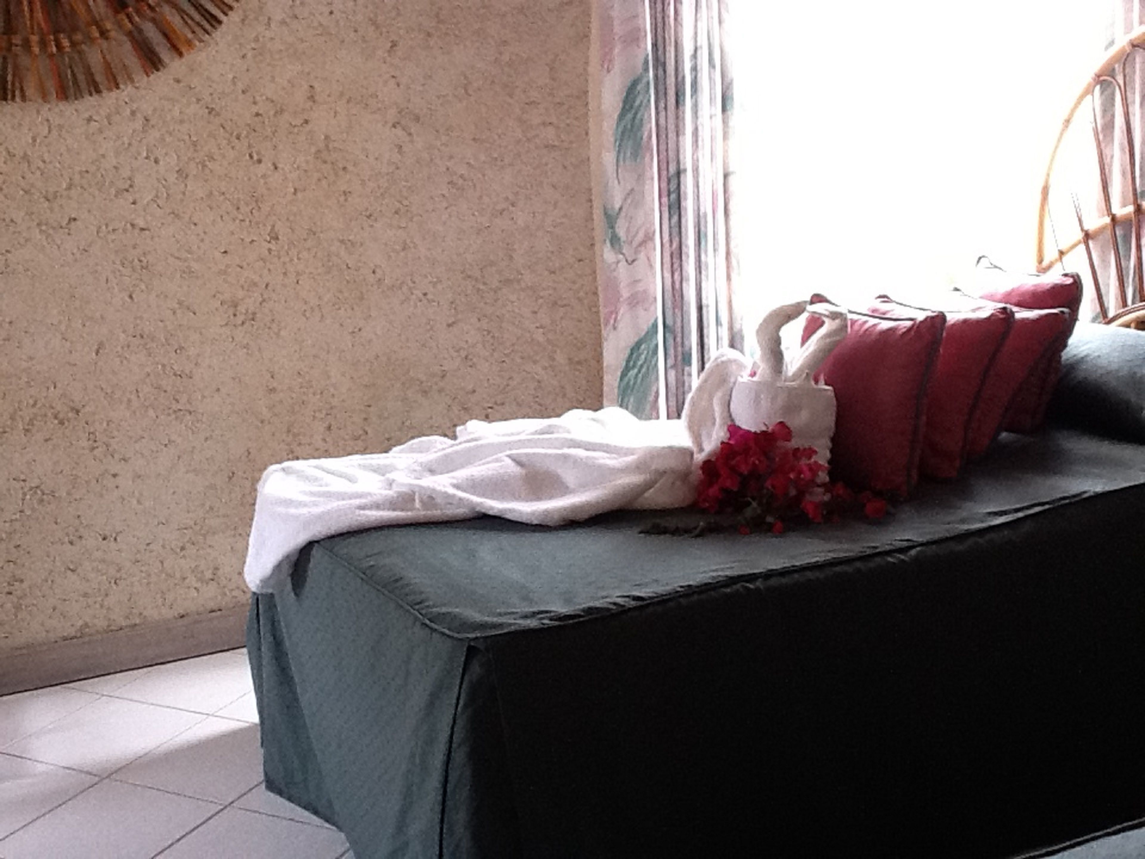 Una habitación con una cama cubierta por una colcha verde, un almohadón con forma de cisne blanco y almohadas rojas.