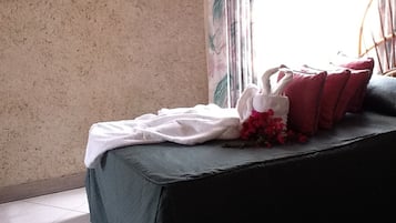 Una habitación con una cama cubierta por una colcha verde, un almohadón con forma de cisne blanco y almohadas rojas.