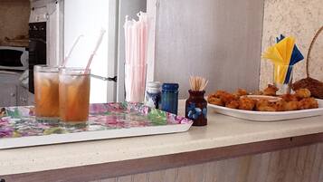 A kitchen counter with a floral tablecloth, two iced drinks, a plate of fried chicken, and a salt shaker.