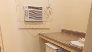 A compact kitchen with a built-in refrigerator, a small countertop, and an air conditioning unit mounted on the wall. - Traveller's Choice Motel (Windsor)