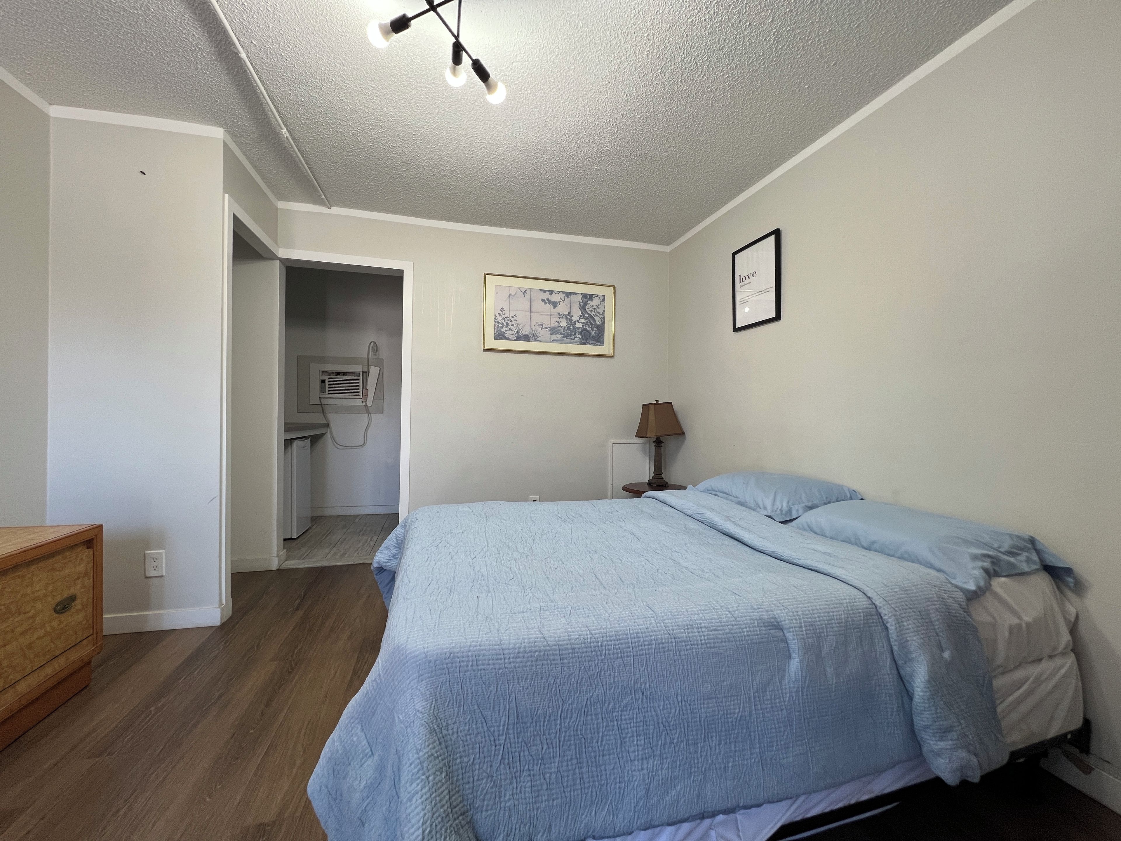 Quarto com cama, abajur, quadro na parede e uma pequena mesa.