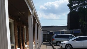 A building with a covered porch, outdoor seating, and a parking area with cars. - Traveller's Choice Motel (Windsor)