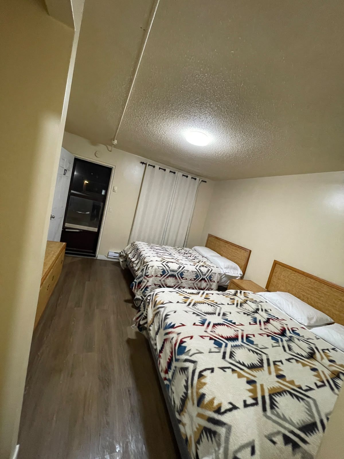 A hotel room with two beds, a wooden headboard, a window with curtains, and a wooden floor.