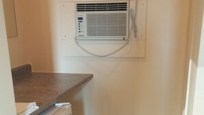 A compact kitchen with a built-in refrigerator, a small countertop, and a wall-mounted air conditioning unit. - Traveller's Choice Motel (Windsor)