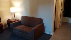 A small, cozy room with a single sofa, a lamp, and a closed door. - Traveller's Choice Motel (Windsor)