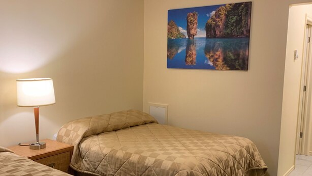 A hotel room with two beds, a nightstand with a lamp, a painting of a landscape, and a door. - Traveller's Choice Motel (Windsor)