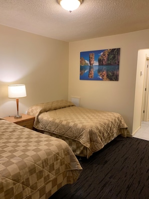 Een hotelkamer met twee bedden, een nachtkastje met een lamp, een schilderij van een landschap en een deur.