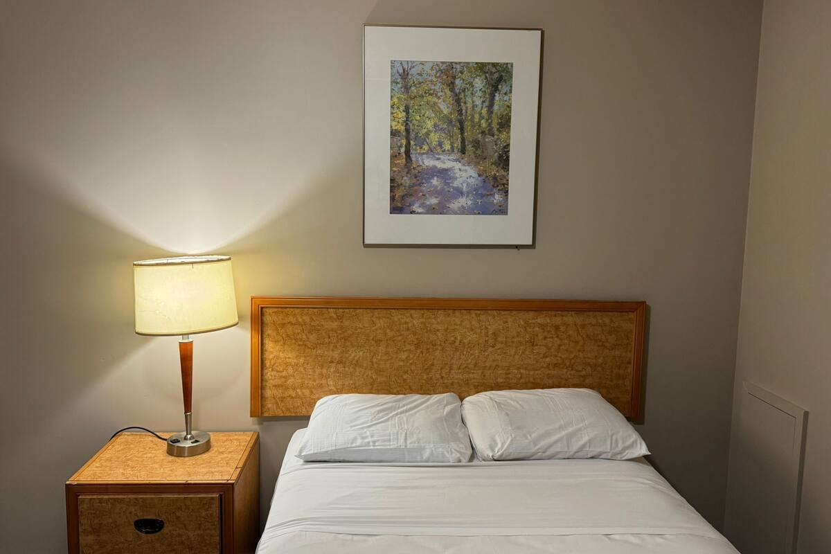 Cama bem arrumada com lençóis brancos, cabeceira de madeira e mesa de cabeceira com abajur.