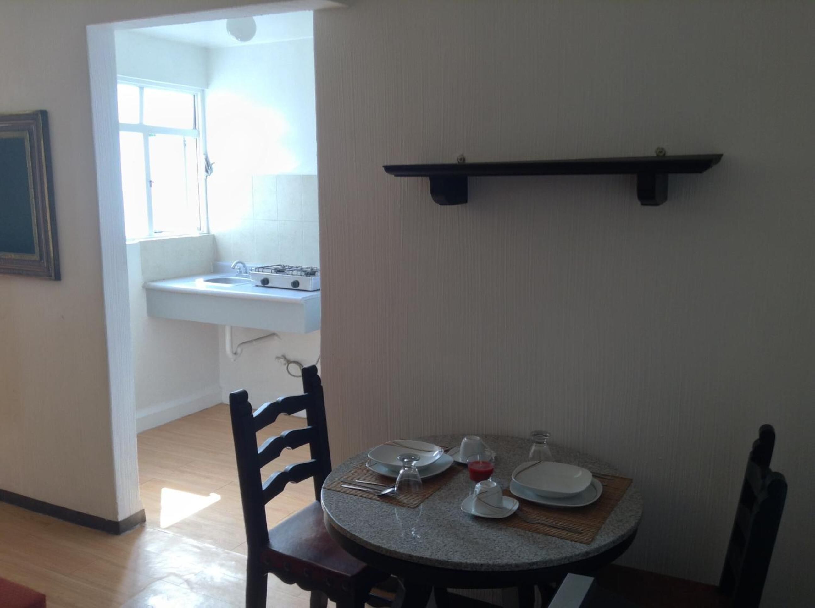 A dining area with a round table set for two, a small kitchen with a sink and stove, and a framed picture on the wall.