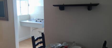A dining area with a round table set for two, a small kitchen with a sink and stove, and a framed picture on the wall.