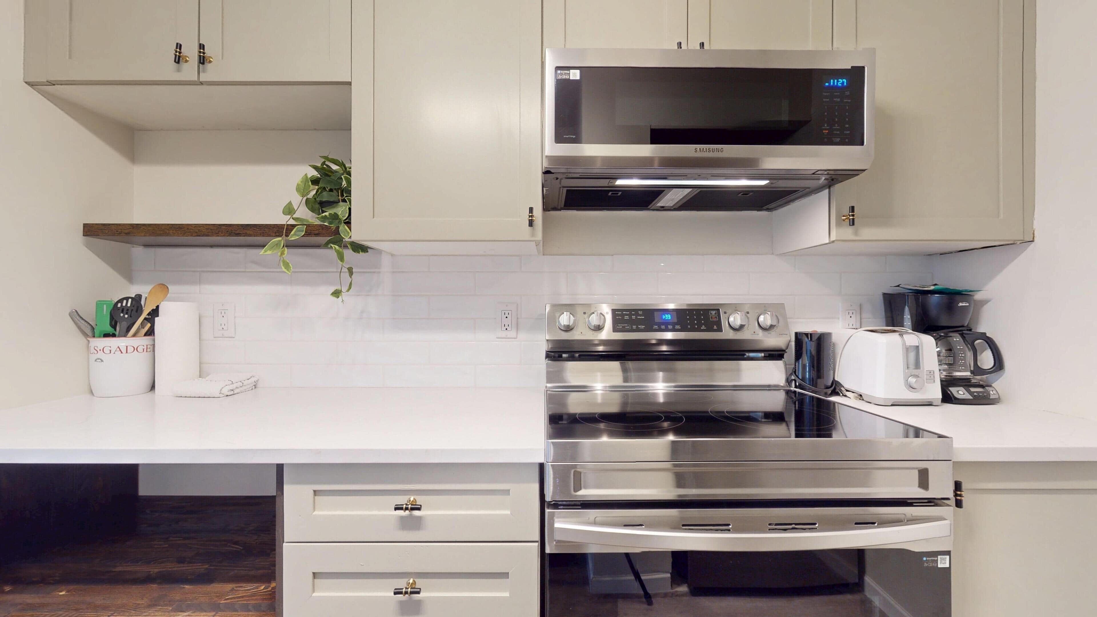 A modern kitchen with stainless steel appliances, including a microwave, oven, and toaster. There is a plant on the counter and a coffee maker.