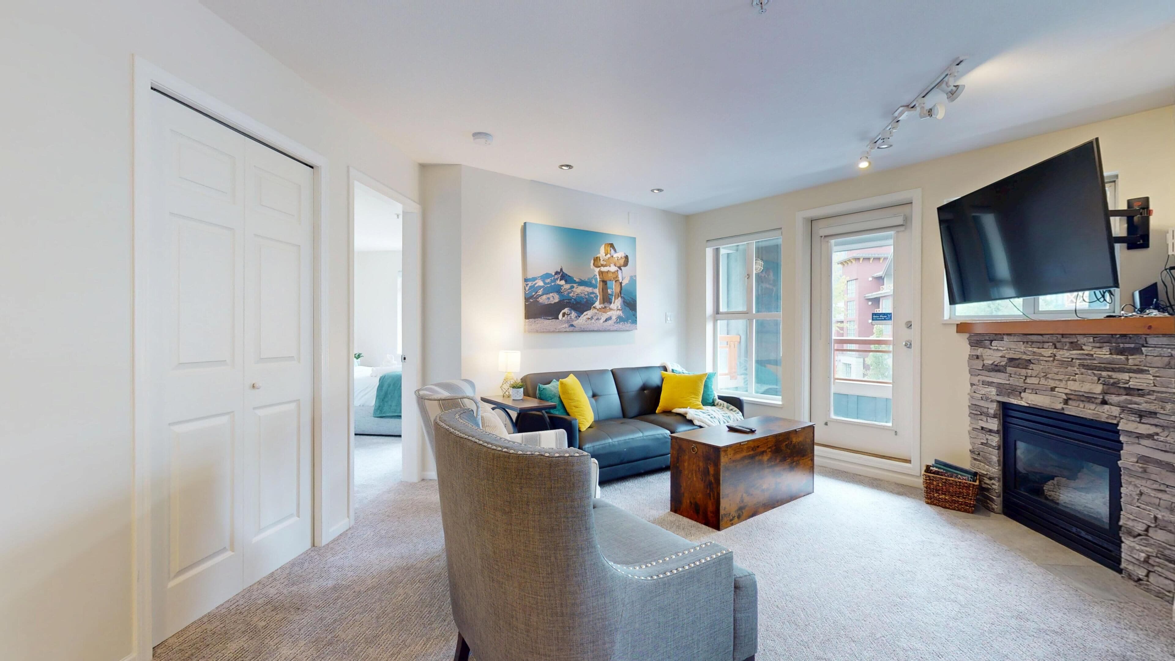 A living room with a stone fireplace, a large flat-screen TV mounted above it, and a sofa with yellow cushions.