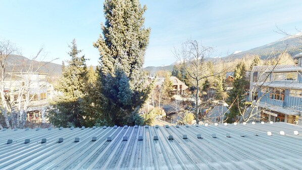 Tejado cubierto de nieve con vista a un pueblo y montañas al fondo.