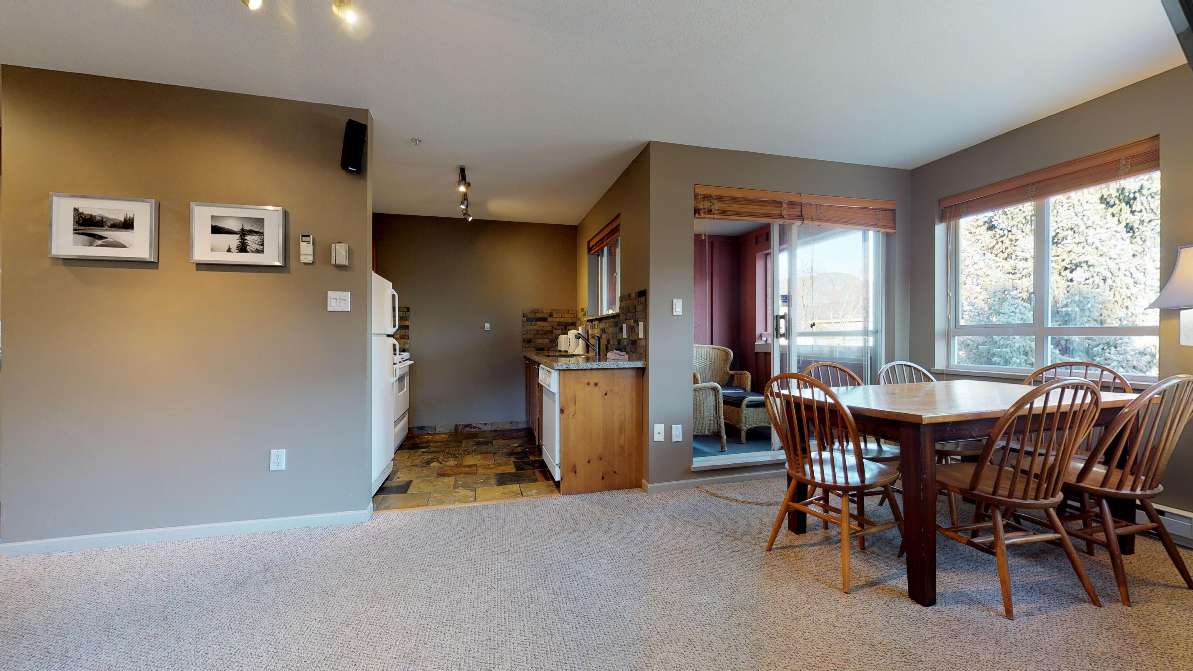 A spacious kitchen with a dining area, featuring a large wooden table and chairs, a built-in oven, and a stone backsplash.