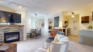 Een moderne woonkamer met een stenen openhaard, een eethoek met tafel en stoelen, een keuken met inbouwoven en een gezellige zithoek met een bank en kussens.
