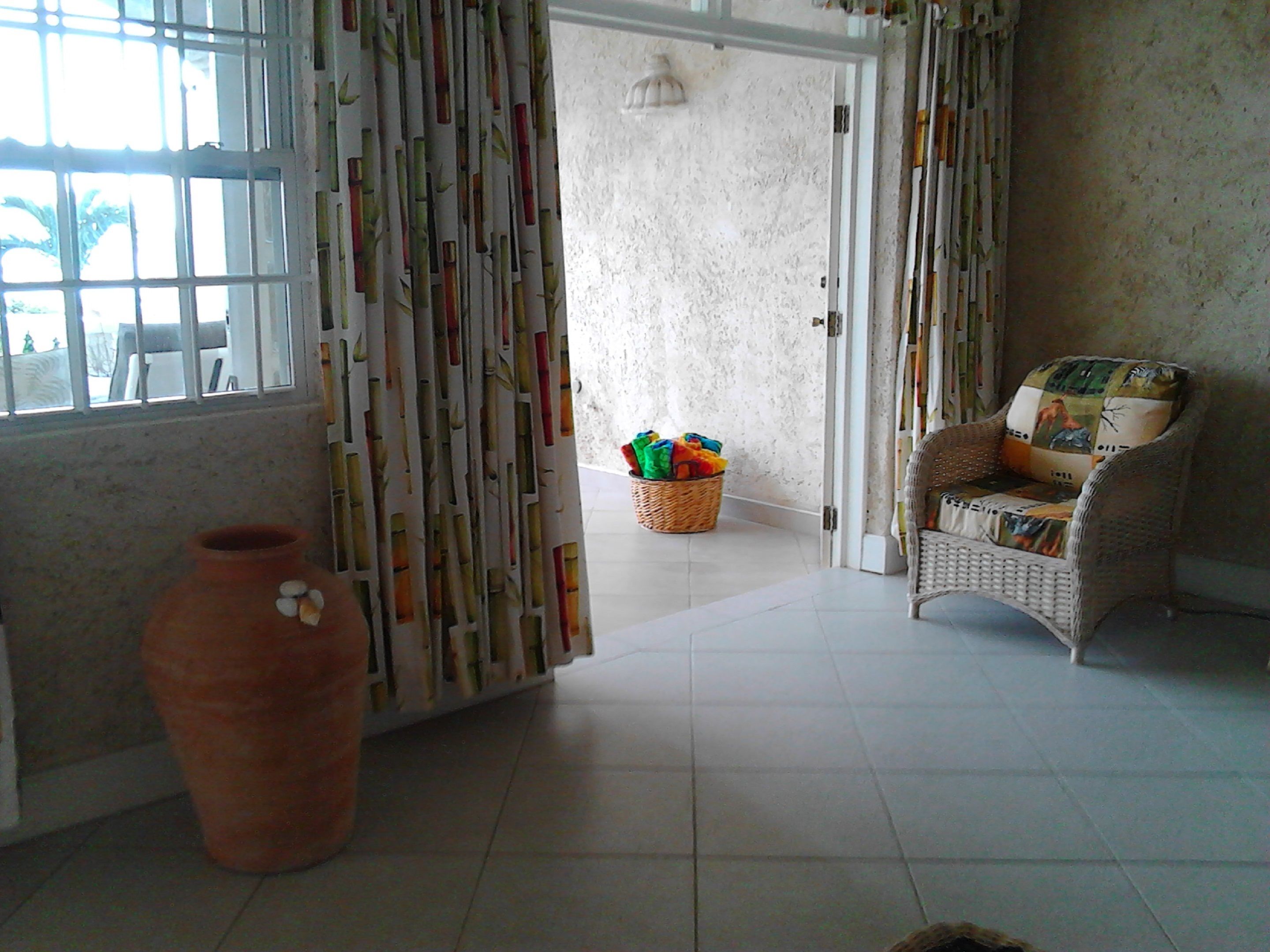 Een kamer met een rieten stoel, een groot raam met behang, een rieten mand met kleurrijke spullen en een terracotta pot.