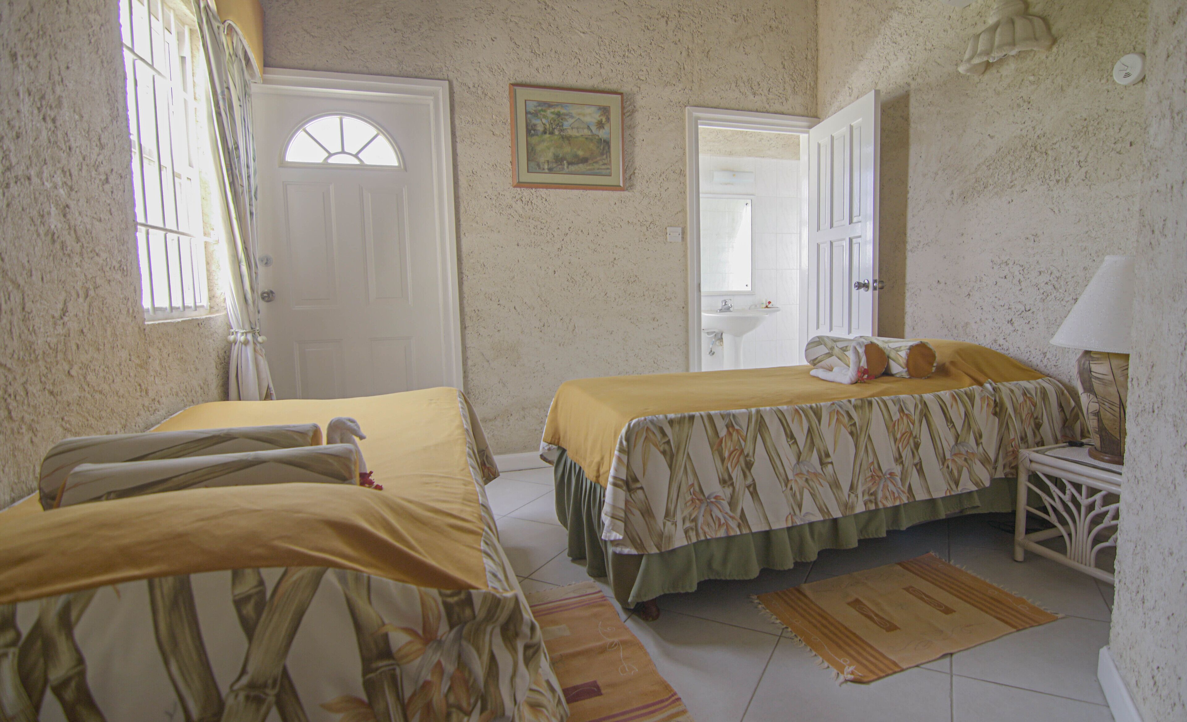 Habitación con dos camas, una mesita, una lámpara, una ventana con rejas y una puerta.