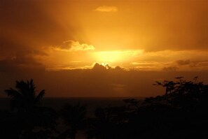 A sunset over a mountainous landscape with silhouettes of palm trees in the foreground. - Seabliss Villa (Fryers Well)