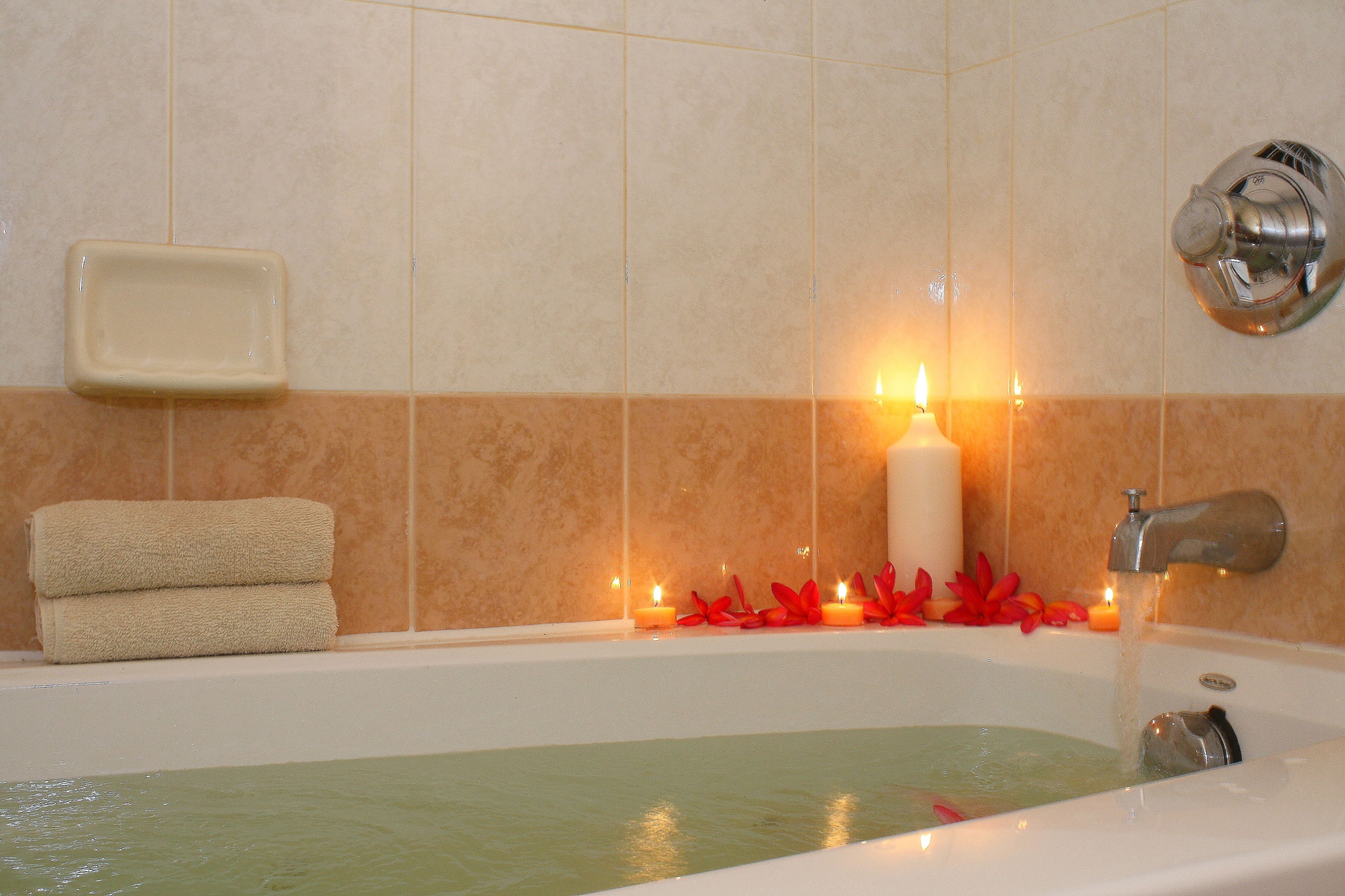 Una bañera con agua corriente, un jabonera y velas en la pared.