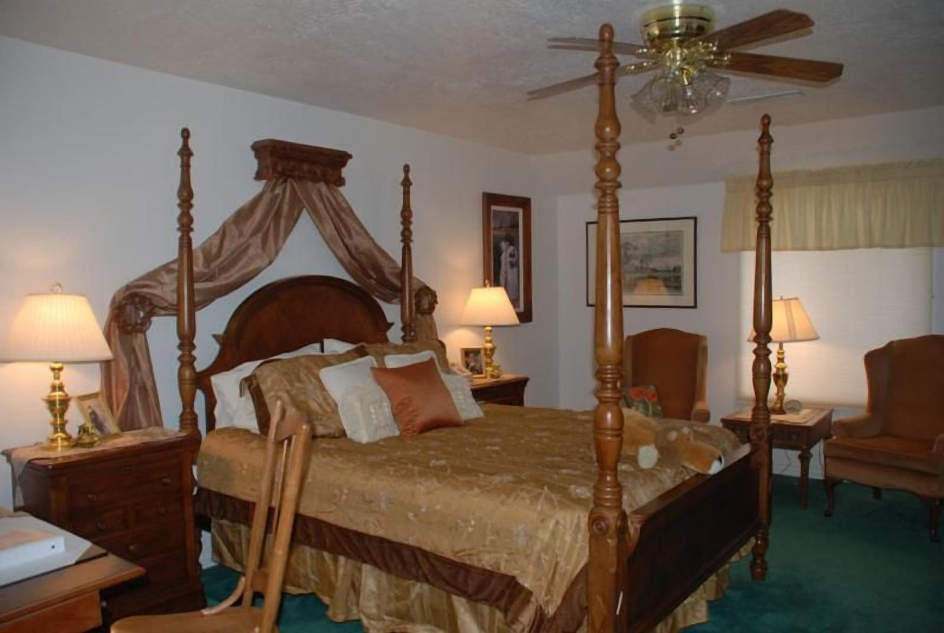 A four-poster bed with a canopy, two bedside tables with lamps, a chair, and a ceiling fan.