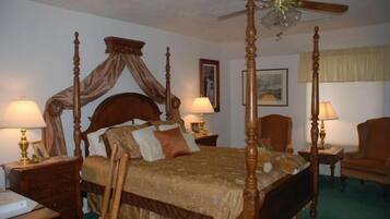 A four-poster bed with a canopy, two bedside tables with lamps, a chair, and a ceiling fan.