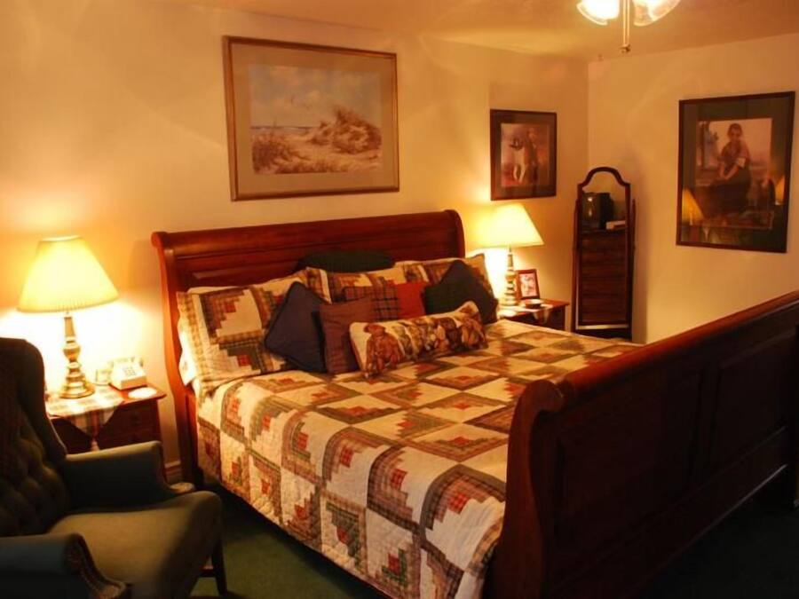 A bedroom with a wooden bed, two bedside lamps, a chair, and framed pictures on the walls.