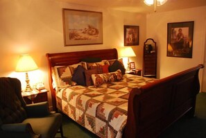 A bedroom with a wooden bed, two bedside lamps, a chair, and framed pictures on the walls.