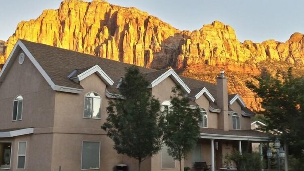 Un edificio de varios pisos con fachada simétrica, amplias ventanas y una imponente montaña al fondo.
