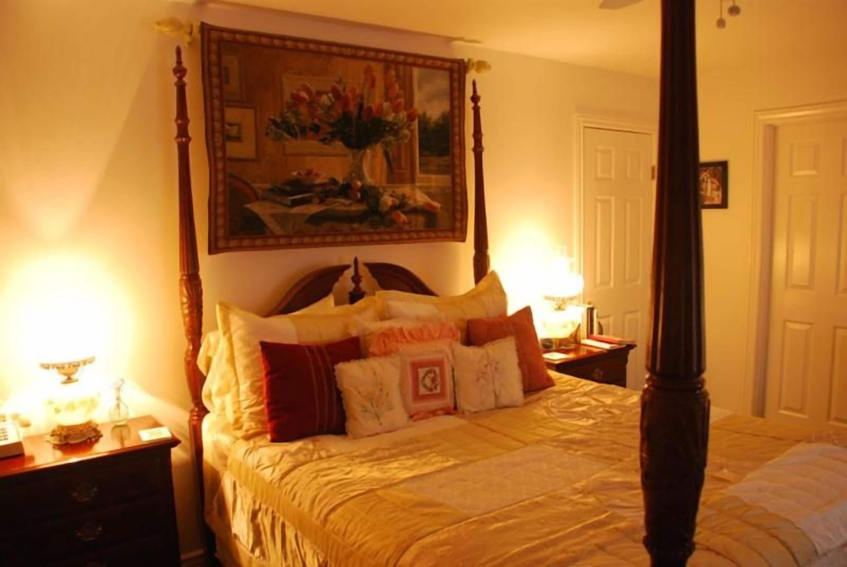 Een hemelbed met hoofdeinde, een nachtkastje met lamp en een ingelijste foto aan de muur.