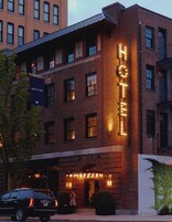 Un hotel con un llamativo letrero de neón, fachada de ladrillo y un cartel con 'NEPTUNE ASH' a la vista al fondo.