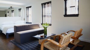 A bedroom with a bed, a sofa, a coffee table, wicker chairs, and a vase with flowers.