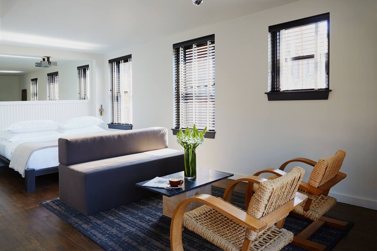 A bedroom with a bed, a sofa, a coffee table, wicker chairs, and a vase with flowers.